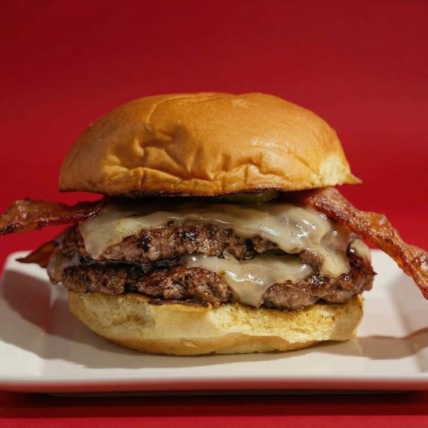 Double patty RedHead Burger with melted cheese and bacon on a white plate against a red background.