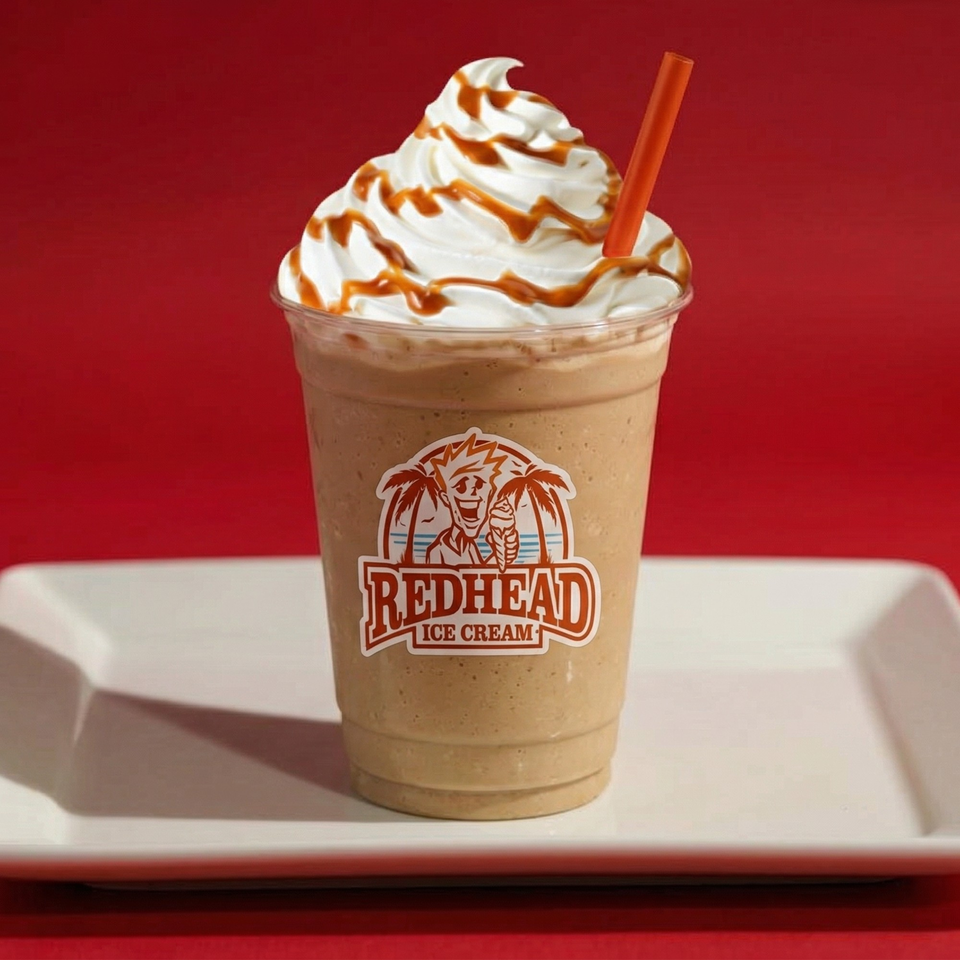 A Redhead Ice Cream milkshake with whipped cream, caramel drizzle, and an orange straw.