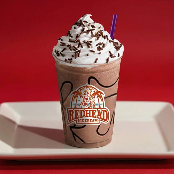 Redhead Ice Cream chocolate milkshake with whipped cream, chocolate sprinkles, and a purple straw.