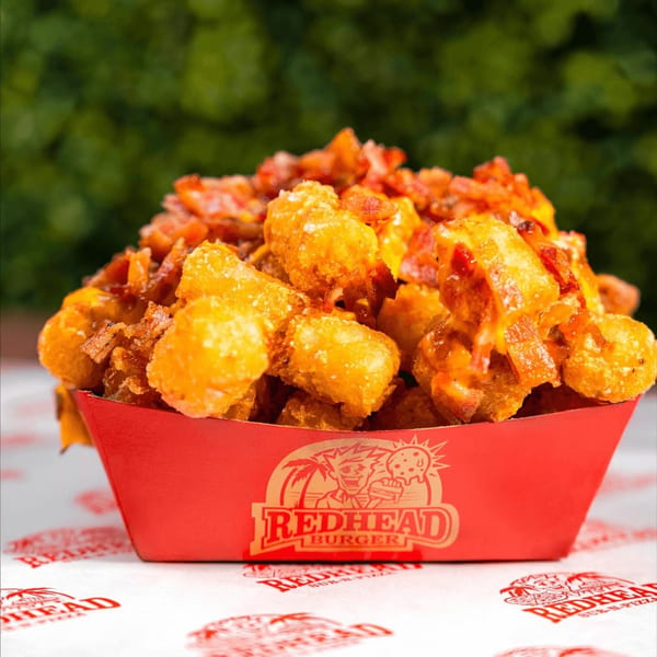 Loaded tater tots with melted cheese and bacon bits in a RedHead Burger branded red tray.