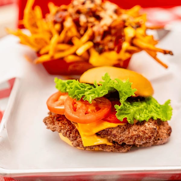 A RedHead Burger with lettuce, tomato, and cheese, next to a basket of loaded fries.