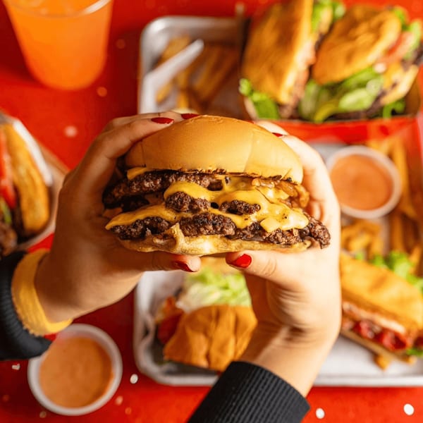 Hands holding a RedHead Burger double cheeseburger with melted cheese and caramelized onions.