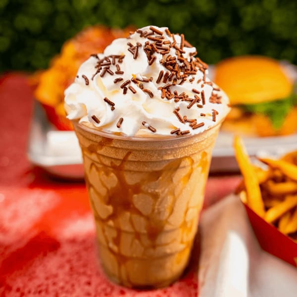 A RedHead Burger milkshake with whipped cream and sprinkles, with fries and a burger in the background.
