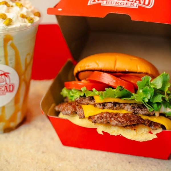 A RedHead Burger with two patties, cheese, lettuce, and tomato, next to a milkshake.