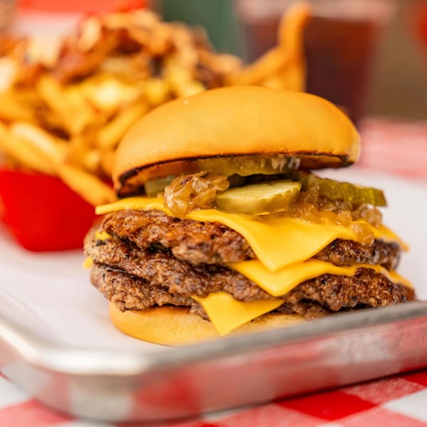 A RedHead Burger double cheeseburger with pickles and caramelized onions, with fries in the background.