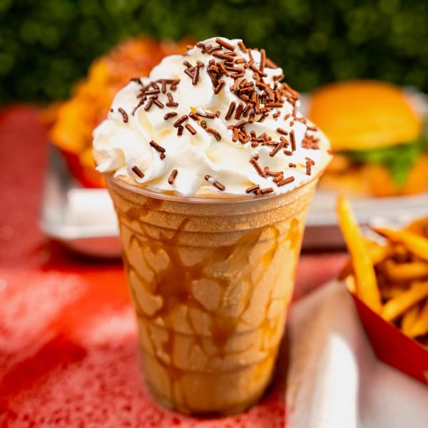 A RedHead Burger milkshake with whipped cream and sprinkles, with fries and a burger in the background.