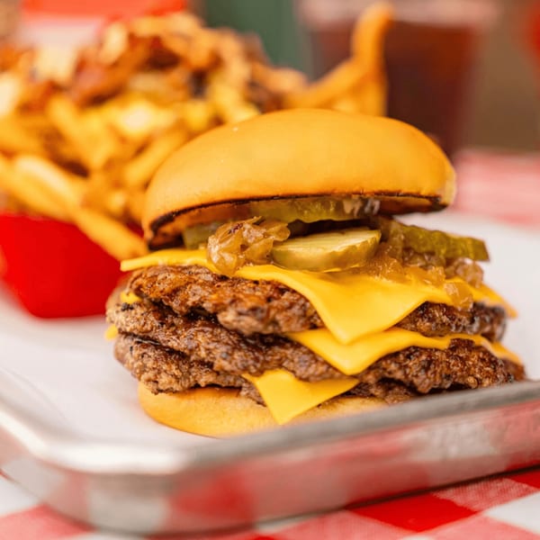 A double cheeseburger with pickles and caramelized onions on a tray with fries.