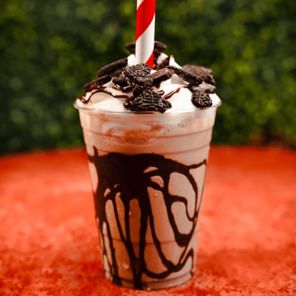 Oreo milkshake with whipped cream, chocolate drizzle, and a red and white striped straw.