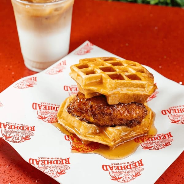 RedHead Burger's chicken and waffles sandwich, drizzled with syrup, next to an iced coffee.