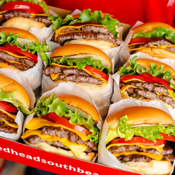 A box filled with many double cheeseburgers, each with lettuce, tomato, and cheese.