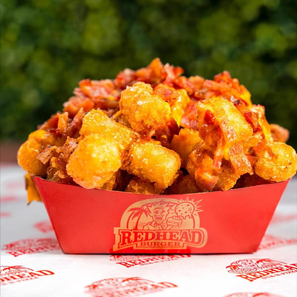 RedHead Burger's crispy tater tots topped with melted cheese and bacon bits in a red tray.